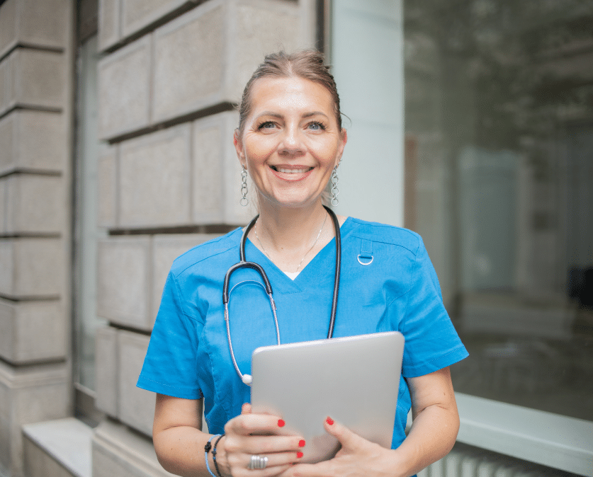 Infirmière libérale souriante tenant une tablette pour gérer la facturation et la cotation des actes selon la NGAP infirmier