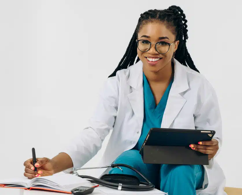 Infirmière souriante en blouse blanche utilisant un logiciel infirmier sur tablette pour gérer les dossiers médicaux