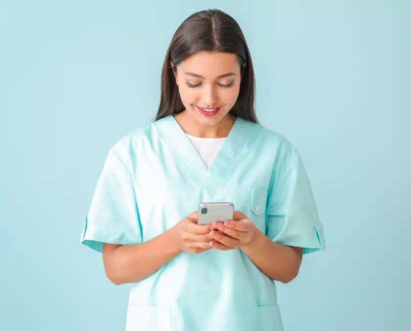 Infirmière en tenue médicale regardant son smartphone pour utiliser un logiciel infirmier mobile
